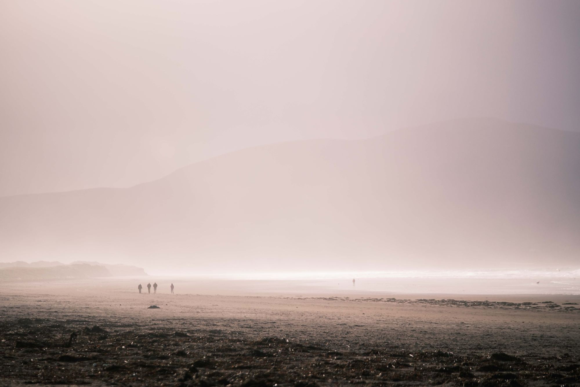 Plage dans la brume, quelques silhouettes marchent au loin