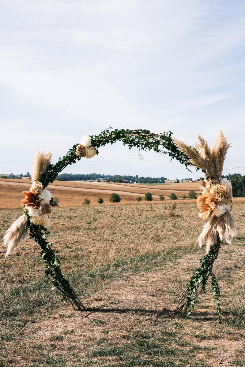 Arche ronde décorée de lierre, de fleurs et d’herbes de la pampa dans un champ