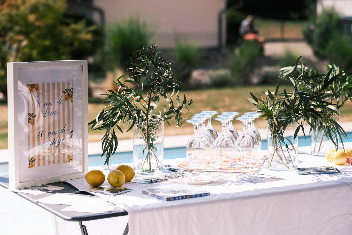 Table d’apéritif au bord d’une piscine, avec un cadre d’anniversaire, des citrons et des verres