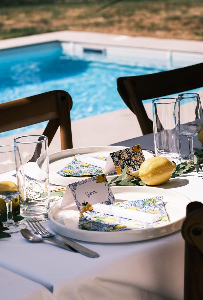Table dressée au bord d’une piscine, marque-places et serviettes aux motifs de citrons