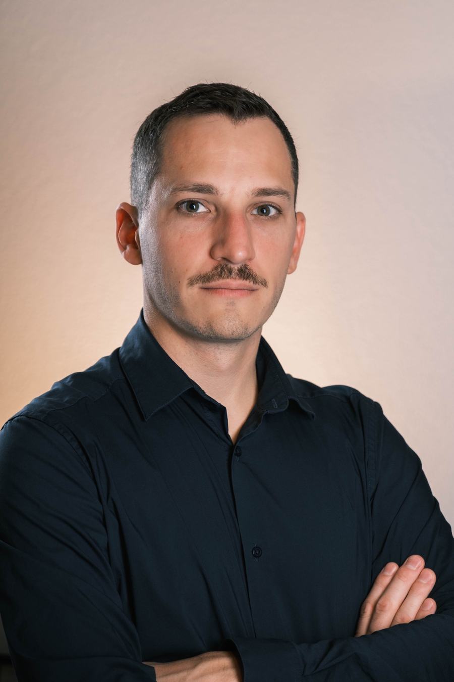 Portrait en studio d’un homme en chemise sombre, bras croisés