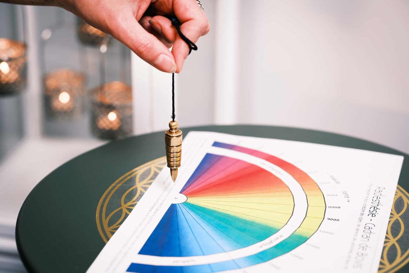 Un pendule doré tenu au-dessus d’un cadran de couleurs, bougies en arrière-plan